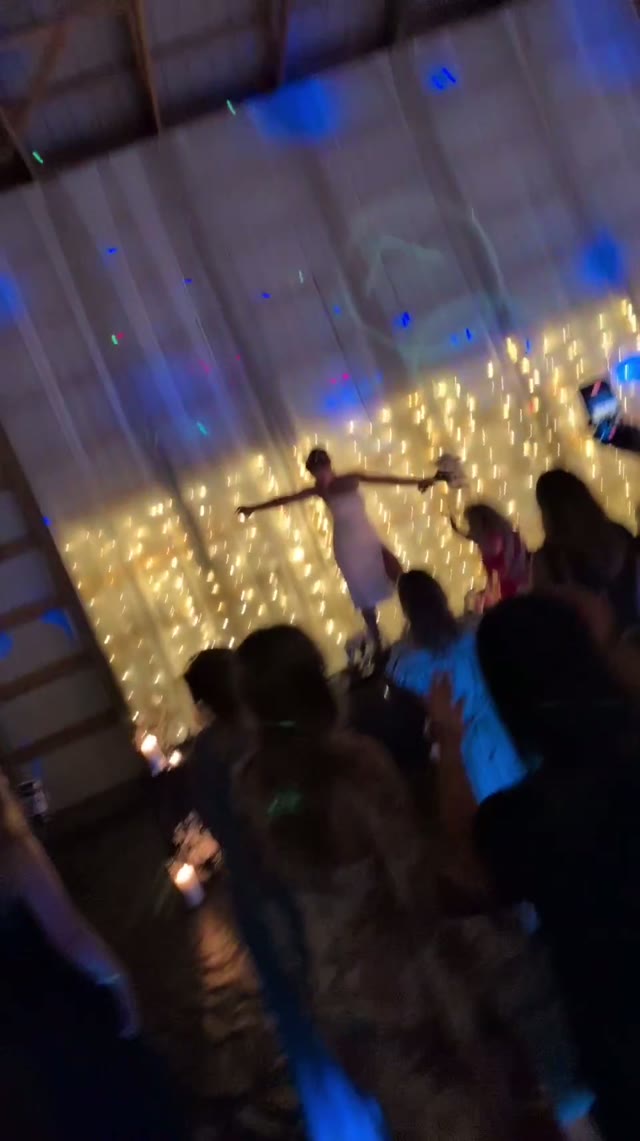 Guests dancing in a barn in front of a curtain wall of fairy lights