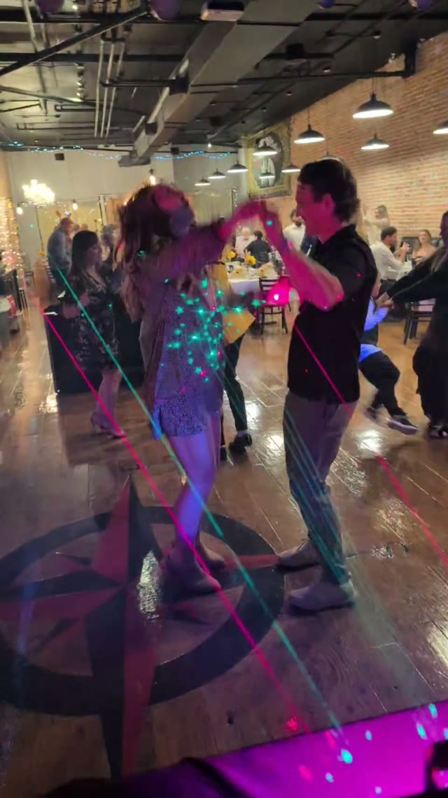 Couples dancing on a compass-star dance floor in a brick-and-beam hall